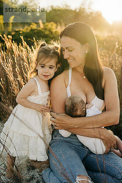 Mother breastfeeding baby while young daughter stands beside them