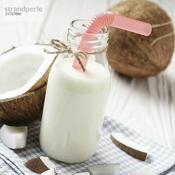 Glass bottle of milk or yogurt on blue napkin on white wooden table with coconut aside