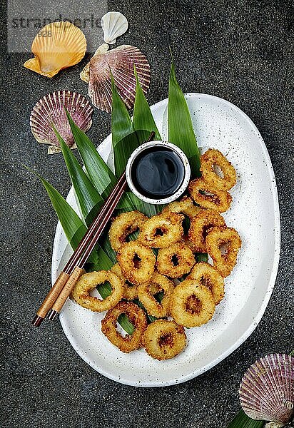 Food  Food  Fried squids rings on white plate decorated with tropical leaves  gray concrete background  top view