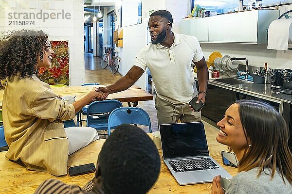 Afrikanischer Mann beim Händeschütteln mit Kollegen in der Cafeteria eines modernen Coworking Centers