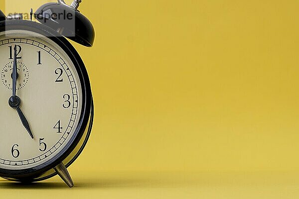 Analog alarm clock displaying five o'clock on a yellow background with copy space. Vintage and retro feel