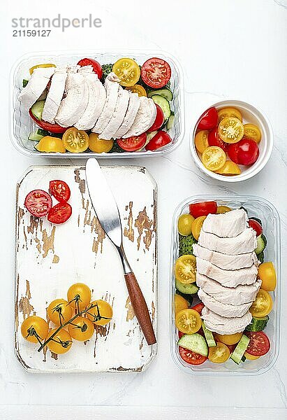 Gesunde Mahlzeit Vorbereitung für das Mittagessen  Diät gekochtes Hühnerfilet mit Gemüse Salat in Lunch Boxen Container Draufsicht auf weißen Marmor Küchentisch Hintergrund mit Messer und Schneidebrett  Lebensmittel Fotografie  food photography  food photography