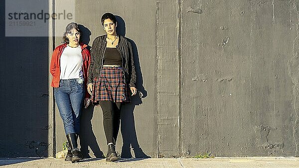 Young lesbian couple leaning against a black wall  looking at the camera with ample copy space