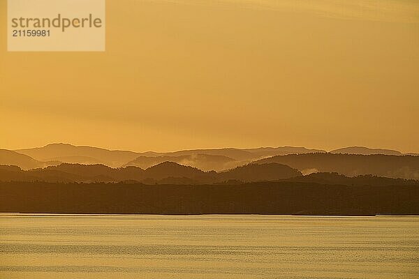 Calm atmosphere over the sea  hills and an orange sunrise  autumn  Bergen  North Sea  Norway  Europe