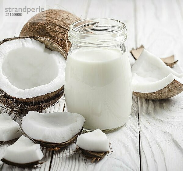 Milk or yogurt in mason jar on white wooden table with coconut aside