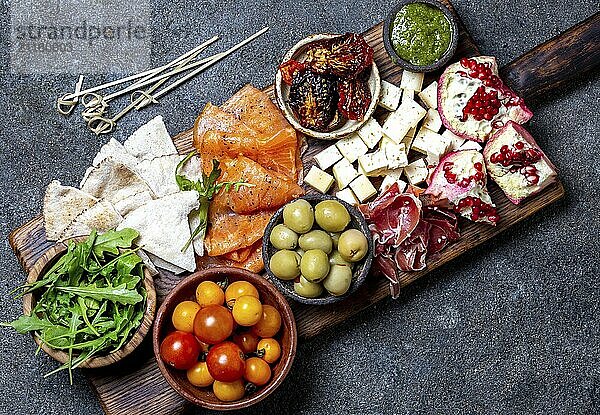 Food  Antipasto. Wine set appetizer. Ham serrano  smoked salmon  dried and fresh tomatoes olive cheese  wine on board. Top view  gray cncrete background