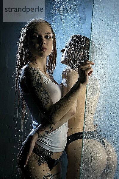 Young tattooed girls having shower together in the dark room