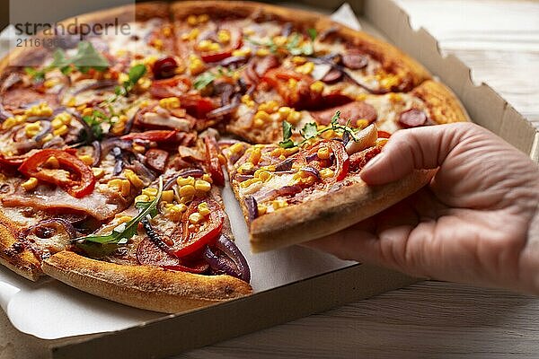 Human caucasian hand takes slice of large pizza from carton box on white wooden table