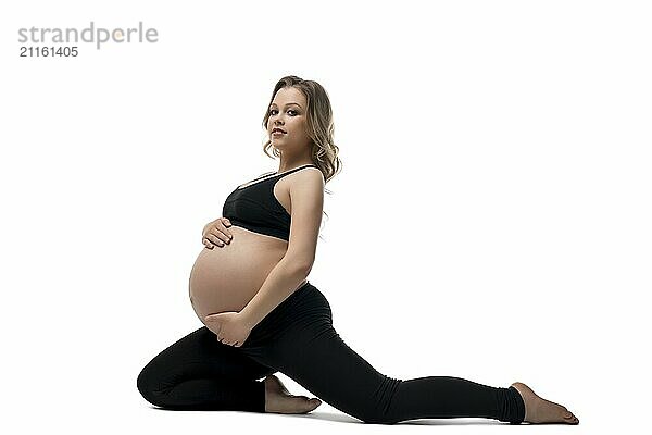 Young pregnant blonde in black sportswear doing fitness sitting in a split isolated profile shot