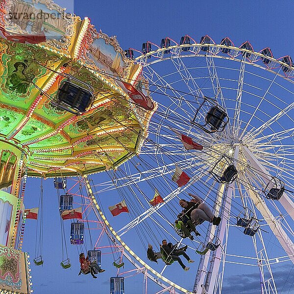 Beleuchtetes Kettenkarussell und Riesenrad bei Nacht mit fröhlichen Menschen  Jahrmarkt  Wellenflug  Cannstadter Volksfest  Stuttgart-Bad Cannstsdt  Baden-Württemberg