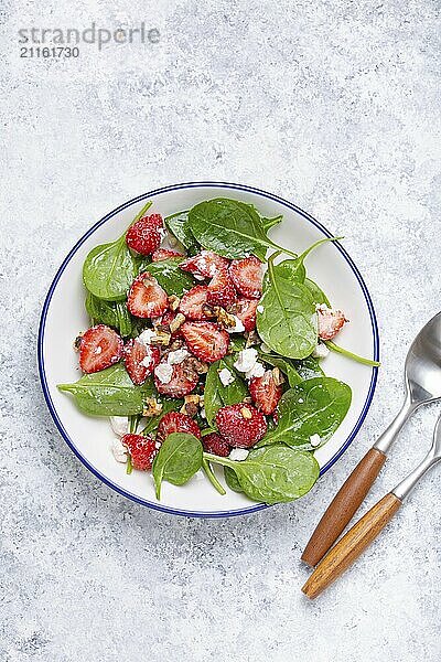 Leichter gesunder Sommersalat mit frischen Erdbeeren  Spinat  Frischkäse und Walnüssen auf weißem Keramikteller  weißer rustikaler Stein Hintergrund von oben  Foodfotografie  food photography  food photography