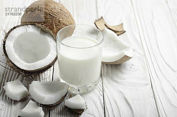 Drinking glass of milk or yogurt on blue napkin on white wooden table with coconut aside