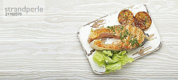 Gegrillter Fisch Lachssteak und grüner Salat mit Zitrone serviert auf weißem Schneidebrett rustikalen hölzernen Hintergrund Draufsicht  ausgewogene Ernährung oder gesunde Ernährung Mahlzeit mit Lachs und Gemüse  Kopie Raum  Lebensmittel Fotografie