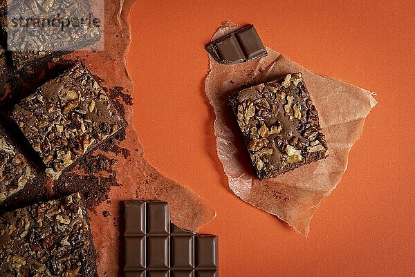 Brownie cake with walnuts sliced in pieces and chocolate chops on baking paper. Directly above view with an orange colored background