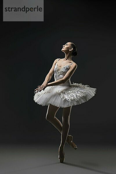 Ballerina wearing white tutu dancing on pointe view in the dark room