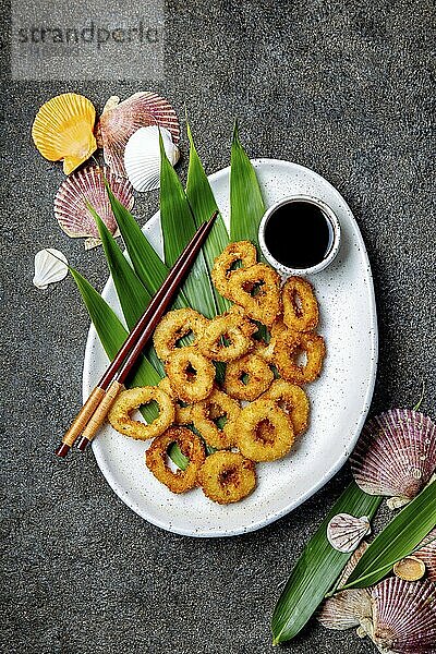 Food  Fried squids rings on white plate decorated with tropical leaves  gray concrete background  top view