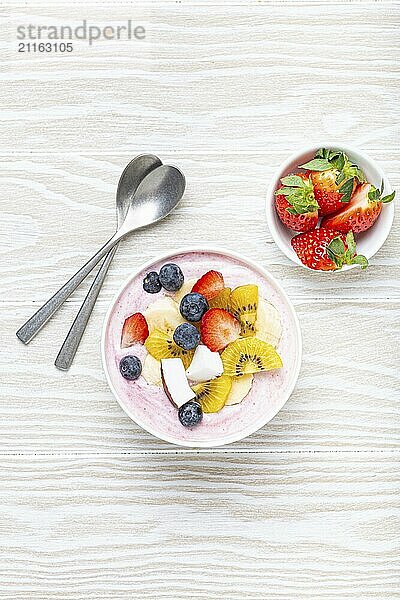 Gesundes Frühstück oder Dessert Joghurt Schüssel mit frischer Banane  Erdbeere  Heidelbeere  Kokos  Kiwi Draufsicht auf rustikalen hölzernen weißen Hintergrund mit Löffel  Lebensmittel Fotografie  food photography  food photography