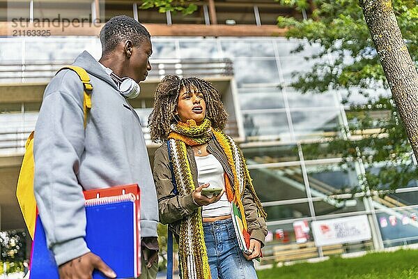 Low angle view photo of two male and female multiethnic students walking along the university campus and talking