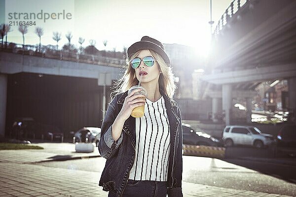 Beautiful girl with juice in sunglass walking at the street on urban style