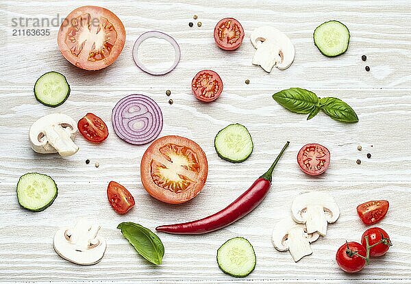 Food cooking background: arranged fresh ingredients  basil  cherry tomatoes  mushrooms  cut cucumber  onion  chilli pepper  spices on white wooden background top view  pattern  food photography