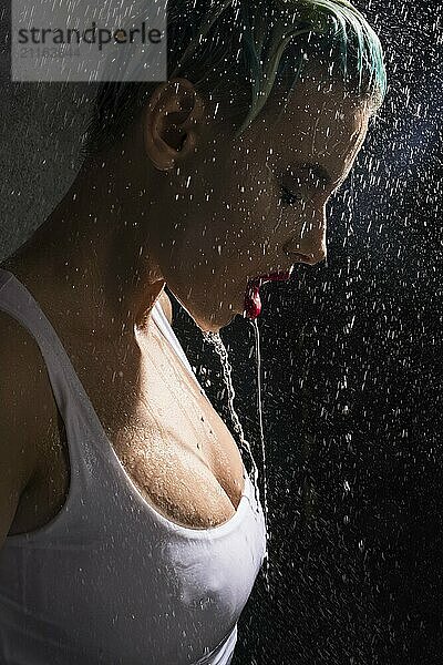 Sexy blonde in top staying under water pouring on her from above in the dark room profile portrait