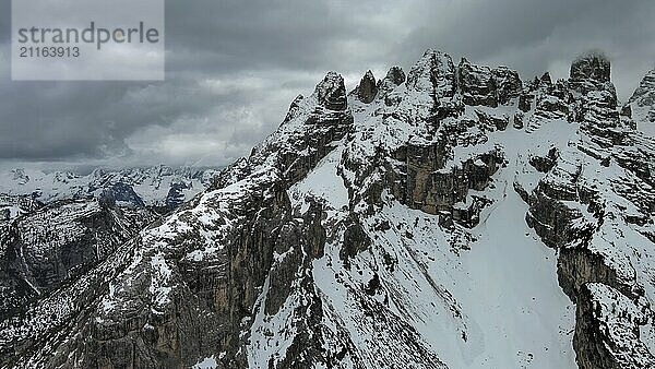 Luftaufnahme von erstaunlichen felsigen Bergen im Schnee unter stimmungsvollen grauen Wolken  Dolomiten  Italien  Europa