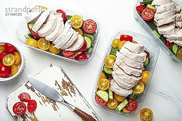 Gesunde Mahlzeit Vorbereitung für das Mittagessen  Diät gekochtes Hühnerfilet mit Gemüse Salat in Lunch Boxen Container Draufsicht auf weißen Marmor Küchentisch Hintergrund mit Messer und Schneidebrett  Lebensmittel Fotografie  food photography