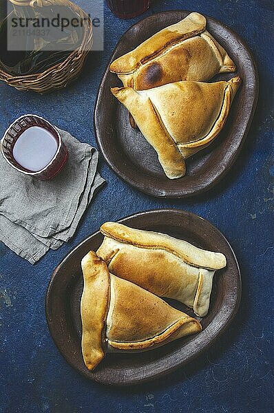 Food  Tipical Chilean baked empanadas de pino y napolitano on clay plates with wine. Dish and drink on 18 September party Independence day Chile  blue background