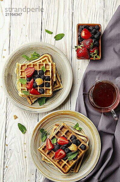 Flat view at belgian waffles served with strawberries and blackberries on white wooden kitchen table closeup