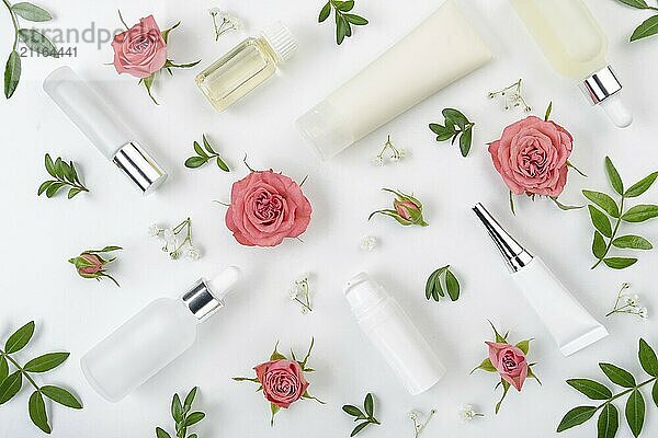 Flat lay kosmetische Flaschen und Behälter mit rosa Rosen und grünen Blättern Hintergrund auf weißem Tisch