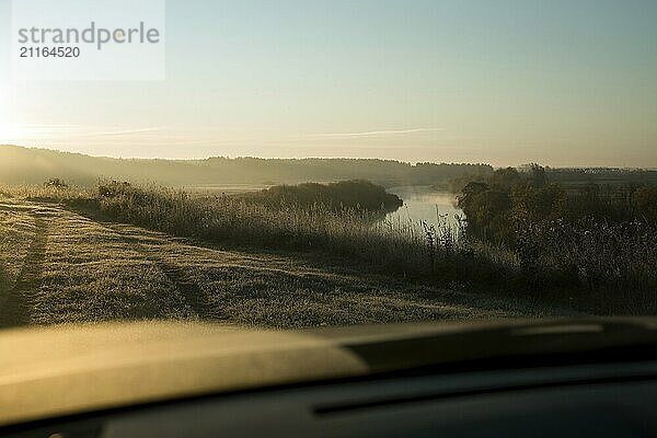 Wunderbarer Blick aus dem Autofenster auf Wiese und Tal mit Fluss und Wald bei Sonnenaufgang mit schönem blauen Himmel