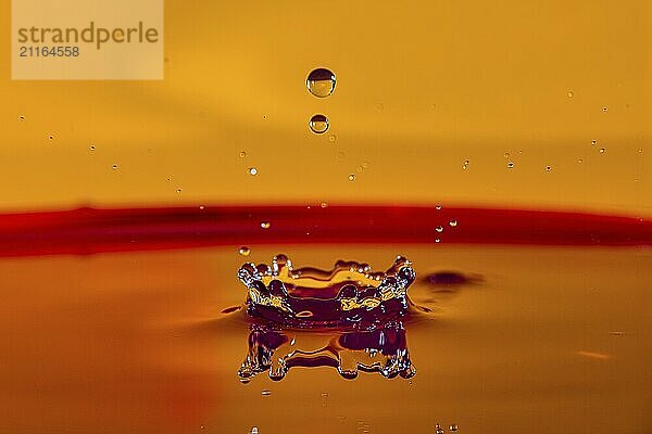 A drop of water creates a crown on a liquid surface with an orange background  high-speed photography  drop photography  Grenzach- Wyhlen  Baden-Württemberg  Germany  Europe