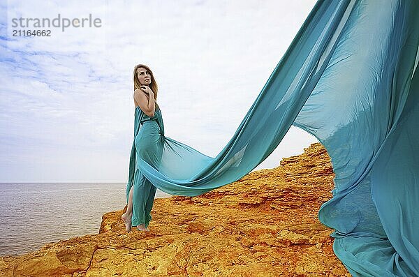 Young beautiful woman in blue dress enjoys sunny day at sea shore