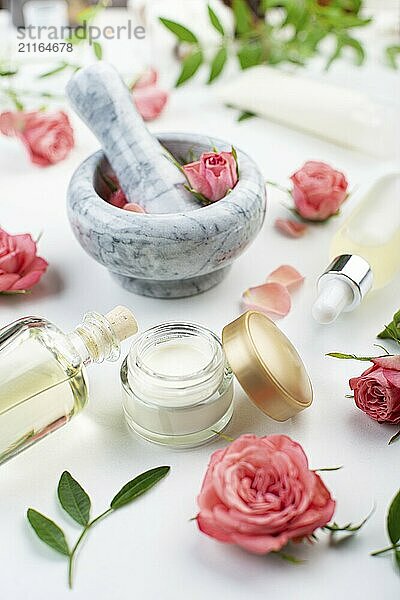 Handmade rose cosmetics concept of mortar and pestle with rose buds with dropper and bottles with serum and oil on white background