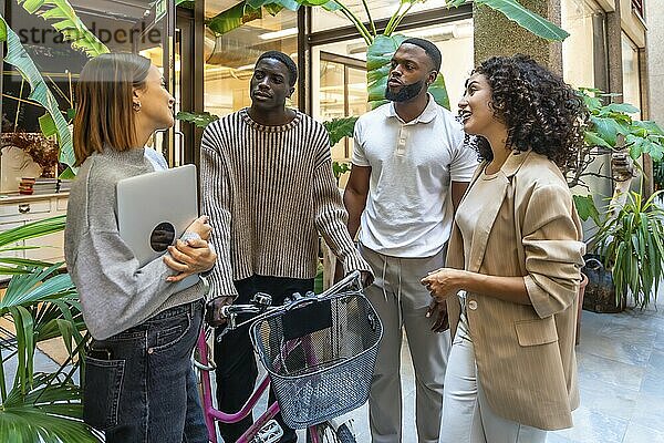 Afrikanischer Mann  der mit dem Fahrrad im Büro ankommt und sich mit Mitarbeitern im Eingangsbereich unterhält