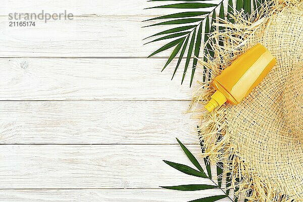 Vacation travel planning simple background of straw hat palm leaves and sunblock lotion on white planks flat lay with copy-space