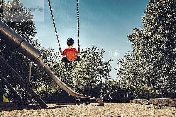 Child swings on playground  surrounded by trees and sunny weather