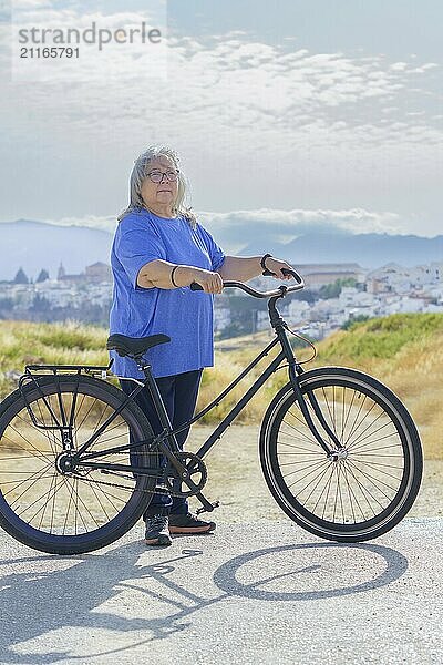 In a mountainous landscape with a village in the background  an overweight white-haired woman rides a retro-style bicycle