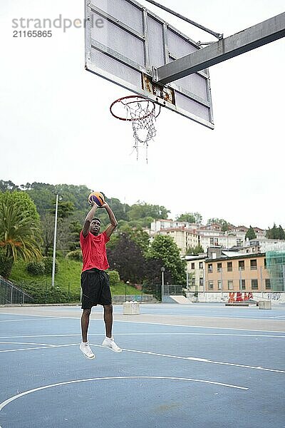 Vertical photo of a basketball player throwing a ball in an outdoor blue basketball court