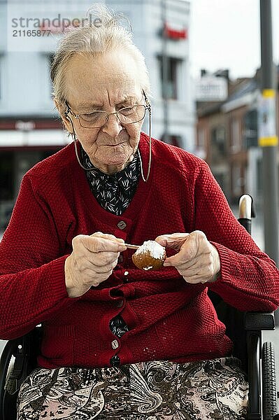 84 jährige Seniorin ißt einen Donut  während sie im Rollstuhl sitzt  Tienen  Belgien  Europa