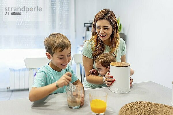 Mother holding a baby and having breakfast with her son at home in the morning