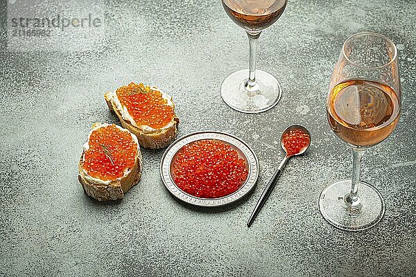 Kleiner Metallteller mit rotem Lachskaviar  zwei Kaviar Toasts Canape  zwei Gläser Champagner von oben auf grauem Betonhintergrund  festliche Luxusdelikatesse und Vorspeise  Foodfotografie