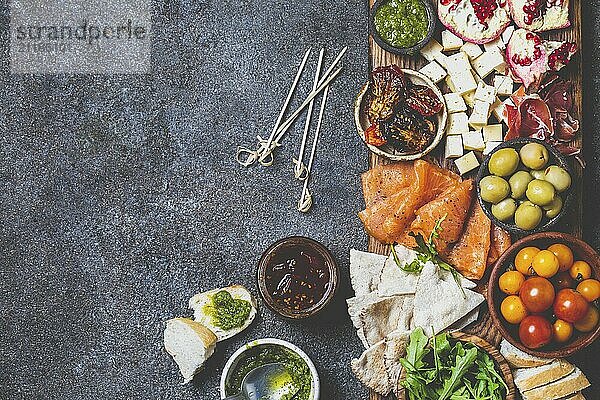 Food  Antipasto. Wine set appetizer. Ham serrano  smoked salmon  dried and fresh tomatoes olive cheese  wine on board. Top view  gray cncrete background