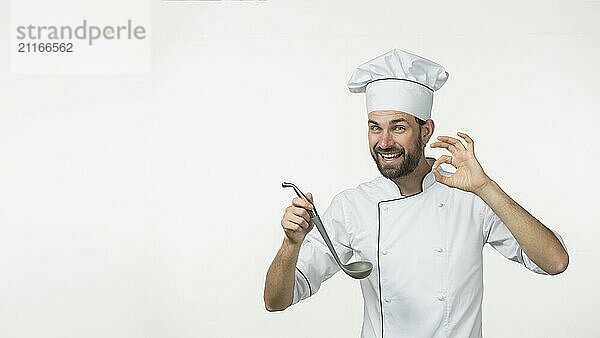 Young male holding soup from ladle making tasty sign isolated white background