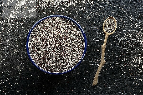 Quinoa Mischung. Gemischte weiße  rote und schwarze Quinoa Samen in einer Schüssel  Overhead Flat Lay Shot auf einem schwarzen Hintergrund  mit einem Holzlöffel  Food Fotografie