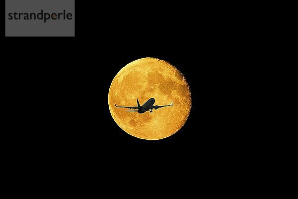 FOTOMONTAGE  Silhouette eines Flugzeugs fliegt vor einem leuchtenden Vollmond am Nachthimmel