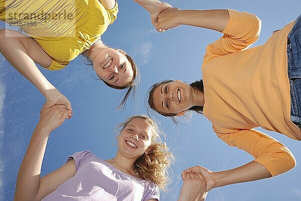 Group of three friends smiling with heads together looking at camera. Low angle view