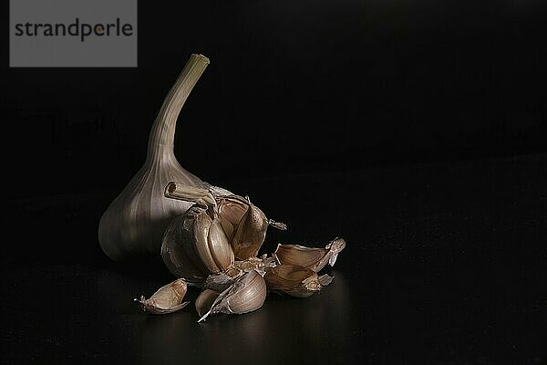 A still life with a whole fresh garlic and garlic cloves on a black background with reflection