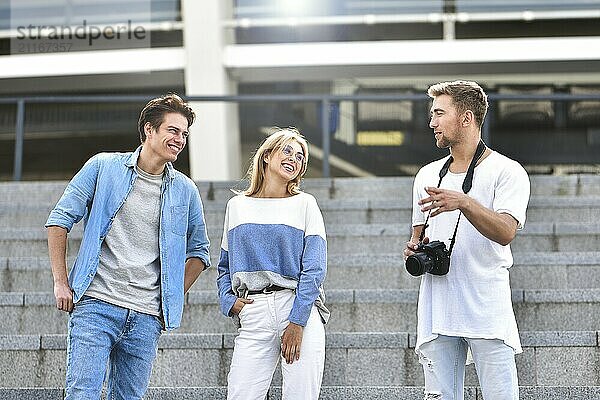 Three happy friends talking taking a conversation on the street in a sunny day with buildings in the background