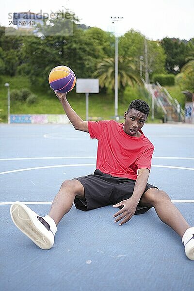 Vertical portrait of an African american basketball player resting sitting on an outdoor court